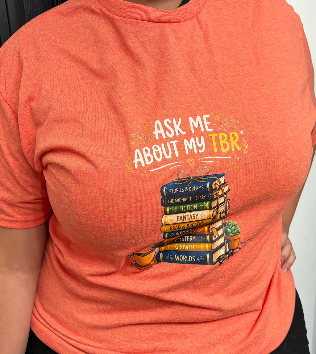 Ask Me About My TBR Tee - orange, front view with stacked books graphic