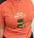 Ask Me About My TBR Tee - orange, front view with stacked books graphic